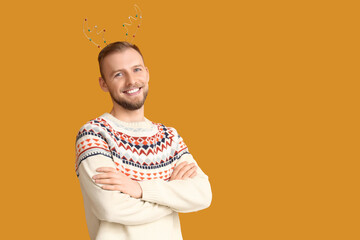 Young man in sweater with Christmas reindeer horns on orange background © Pixel-Shot