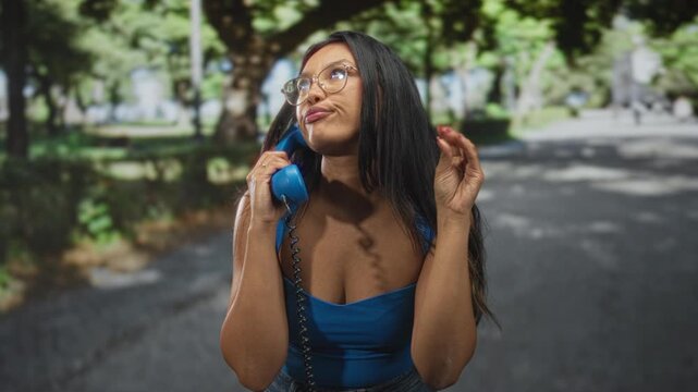 Young hispanic woman holding vintage telephone handset to ear while making a dismissive hand gesture on a street; sassy attitude.