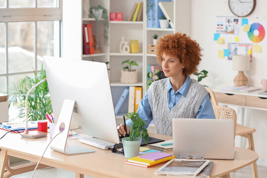 Redhead female graphic designer working at table in office