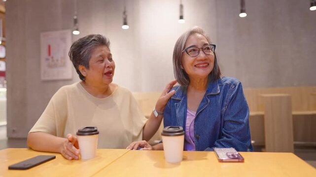 Two Asian senior women laughing and talking to each other in restaurant.