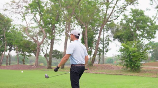 Asian young male golfer walk across lush green fairway with golf club. 