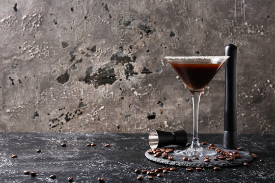Glass of tasty espresso martini cocktail, bartender tools and coffee beans on grey grunge background