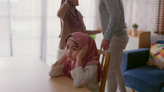 Adorable Muslim girl covering ears while parents argue in background.