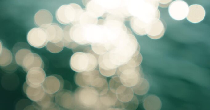 Blurred bright sunlight reflection creates round bokeh patterns on deep green blue water surface