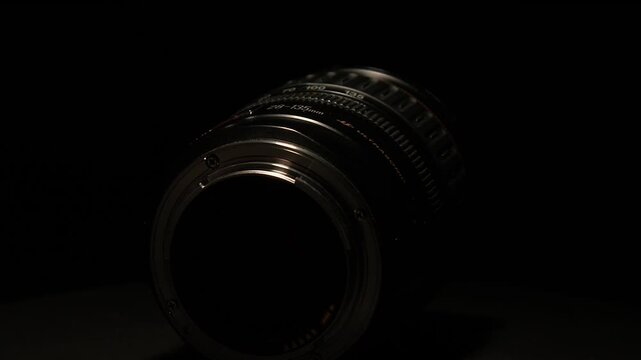 Macro detail: Zoom lens revolves in black room, dimly light from above