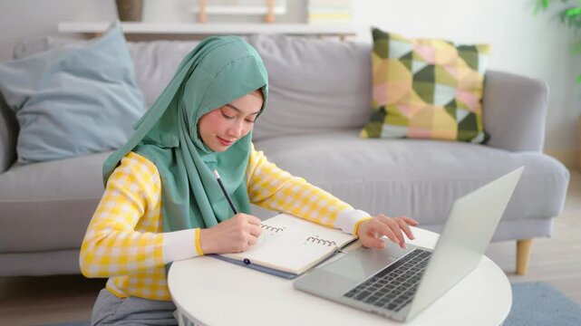 Asian Muslim woman student learning online class in living room at home.