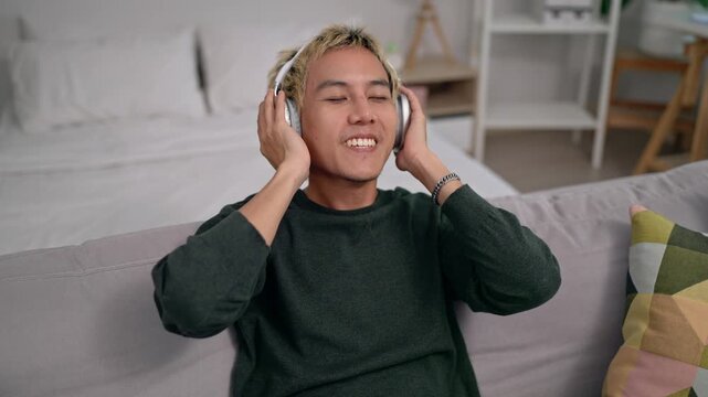 Asian man wearing headphones and softly nodding his head to the beat. 