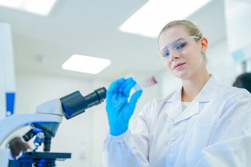 Fototapeta premium Professional female scientist in white lab coat and goggles working with automated laboratory equipment. Expert researcher analyzing clinical samples for biotechnology and medical development.