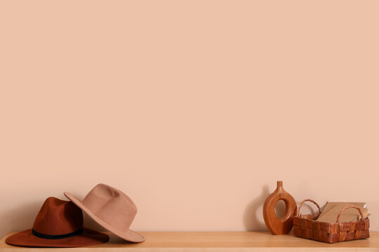 Stylish hats with books and vase on shelf near beige wall