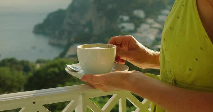 Cup of cappuccino held above Marina Piccola view in Capri Italy during warm summer morning