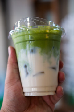 Refreshing iced matcha latte with milk layer on man hand