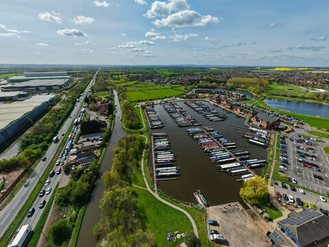 Aerial view of Barton Marina with narrowboats moored in rows next to the canal and a busy road under a cloudy sky Barton-under-Needwood, England, United Kingdom.