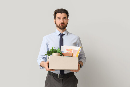 Fired young man holding box with personal stuff on light background