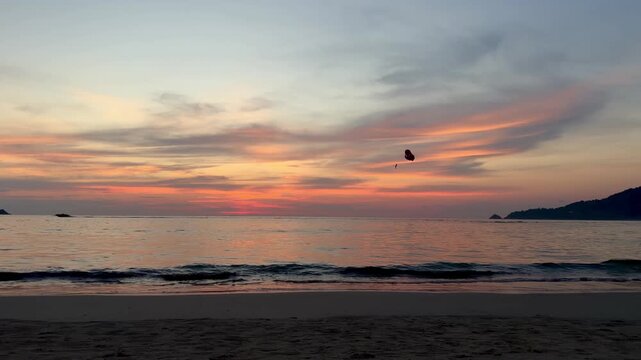 Scenic view of a faraway parachute over the sea and coastal green mountains at Patong beach in Phuket. Beautiful sunset horizon, calm ocean waves and tropical evening nature landscape in Thailand.