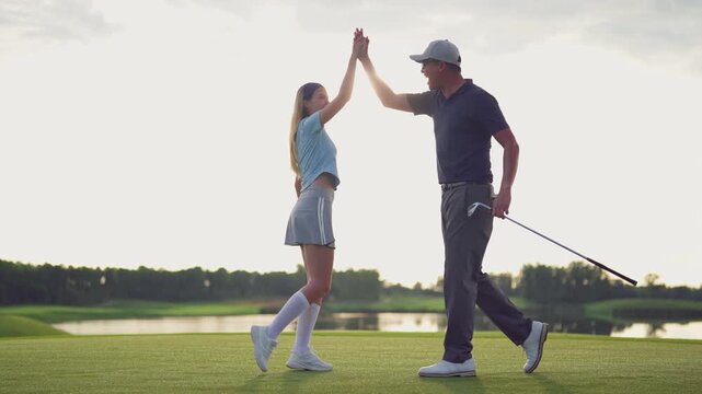 Asian man and woman golfers making a high five on scenic golf course. 