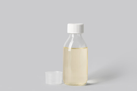 Bottle of cough syrup and measuring cup on grey background