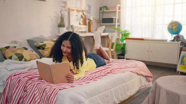 African American teenage girl lying on comfort bed and reading a book. 