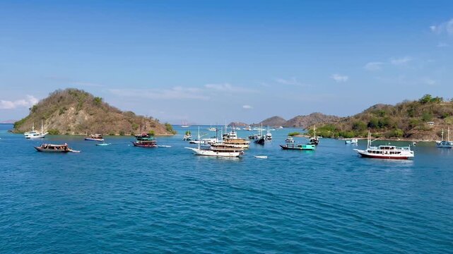 Cinematic horizontal panning shot of beautiful tropical bay in labuan bajo with phinisi ships and yachts anchored near green hills