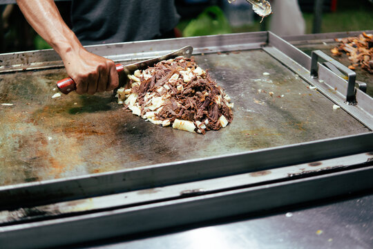 Hand chopping street food meat on griddle