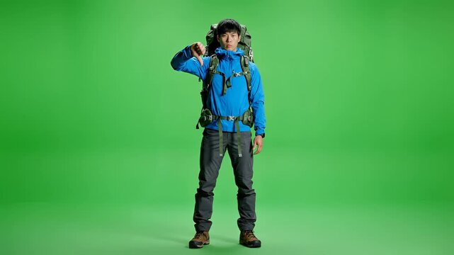 Young hiker in blue jacket with backpack on green screen background.