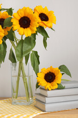 Naklejka premium Vase with sunflowers and books on shelf near light wall