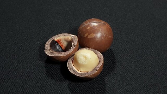 Whole and cracked macadamia nuts on black background.