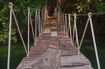 Fototapeta premium A rustic wooden suspension bridge spanning a verdant river