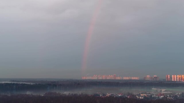 Panoramic view of a vibrant rainbow over Mitino district buildings in Moscow, Russia. Beautiful morning fog mist over forest trees, real estate apartments and scenic urban landscape background.
