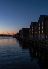 Fototapeta premium Industrial cityscape featuring dark brick buildings along a harbor at dusk with blue hour lighting and water reflections for real estate development background