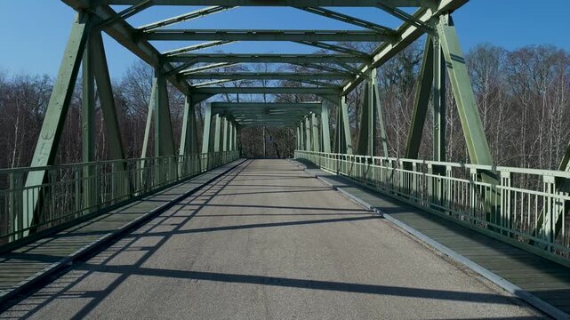Crossing empty green metal truss bridge over a forest