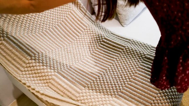 Woman Spreading a Textured Beige Woven Rug Over a White Sofa