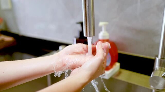 Person Washing Hands with Soap Under Running Water in Kitchen Sink