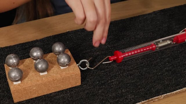 Spring scale measuring friction force on cork block with lead weights during physics experiment.