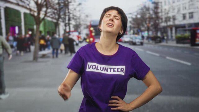Volunteer woman wearing purple volunteer tee with hand to forehead and hand on hip on street, eyes closed in grimace; frustration.