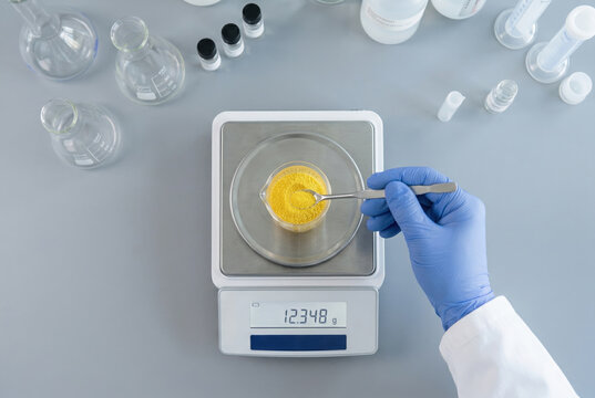 Scientist weighing bright yellow chemical powder on a digital scale inside a laboratory