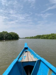 Naklejka premium Travel by Indonesia. Bow of traditional wooden longtail boat sailing tropical river with mangrove forests around the river and Clear Blue sky cloudy