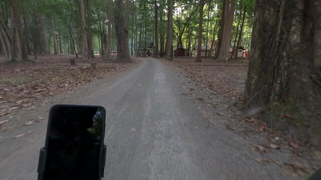 POV riding a scooter towards the entry to Kong Lor cave, through a forest area on a gravel road.
