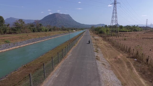 Aerial tracking shot behind a scooter as a man rides along the road towards Kong Lor on the Thakhek Loop.