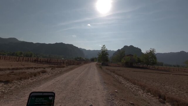 POV summertime riding along a bumpy road towards karst limestone formations on the Thakhek Loop in Laos.