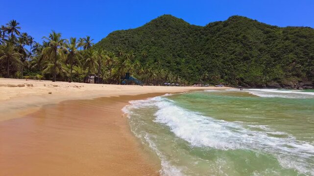 Panoramic view of the large beach at Choroni, with crystal-clear turquoise waters, palm trees along the shore, and green mountains in the background, Aragua, Venezuela