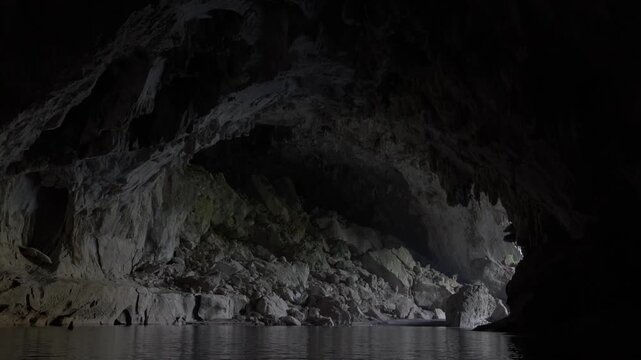 Tilt down reveal from on the underground river of the exit of Kong Lor cave as sunlight shines in.