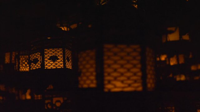 Close-up detail of traditional Japanese lanterns illuminated by candles at Kasuga Taisha Shrine in Nara, Japan. The ancient lamps feature intricate kanji and deer engravings, casting a warm glow in th