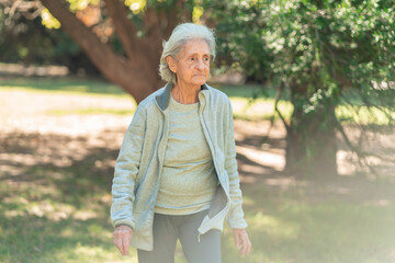 A senior woman with white hair enjoys a walk through a park, dressed in a fleece jacket and leggings for comfort on a chilly day © Jezabel