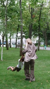Vertical video. Swinging family fun. Carefree lifestyle. Mother son actively spinning holding hands in park happy summer interaction.