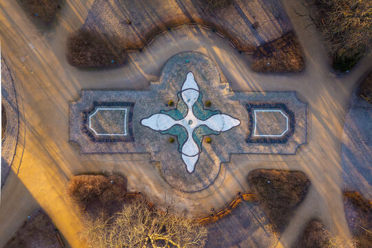 Aerial view of a symmetrical garden feature with intricate patterns and gravel paths surrounded by bare trees in a park during golden hour in Warsaw, Masovian Voivodeship, Poland.
