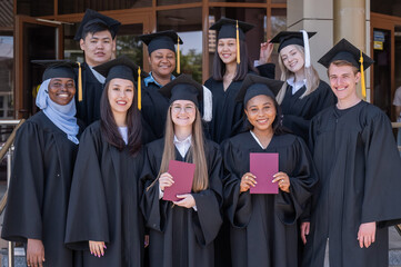 Obraz premium Happy students of different nationalities in graduation gowns hold their diplomas.