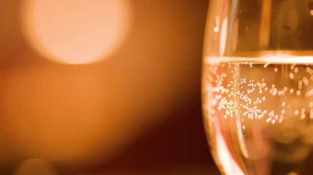 Macro of champagne flute with rising bubbles and warm orange lighting bokeh background.