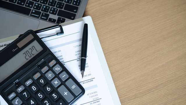 Office desk with calculator, pen and financial paperwork near laptop, accounting and finance planning concept with minimal composition and copy space.