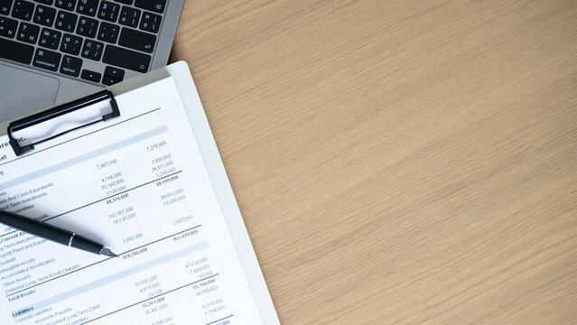 Business financial report with laptop, clipboard and pen on wooden desk, office accounting workspace with copy space for budget, audit and finance concept.