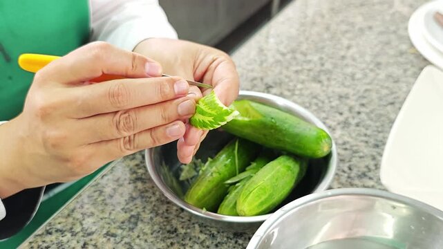 Close up of woman's hands delicately carving a cucumber into a leaf shape.